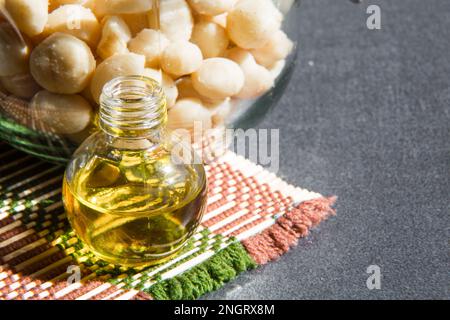 Still life with Macadamia oil in the bottle and nuts in the jar on the grey background Stock Photo