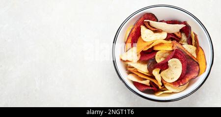 Bowl of mixed healthy vegetable chips isolated on a white background. Top view. Panorama with copy space. Stock Photo