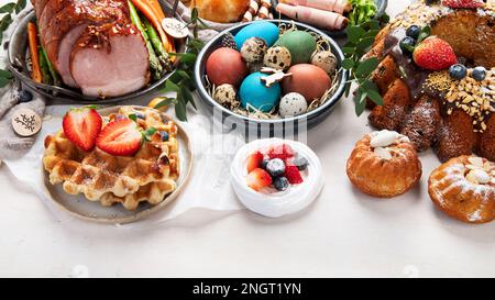 Traditional Easter dinner or  brunch with ham, colored eggs, hot cross buns, cake and vegetables. Easter meal dishes with holday decorations. Stock Photo