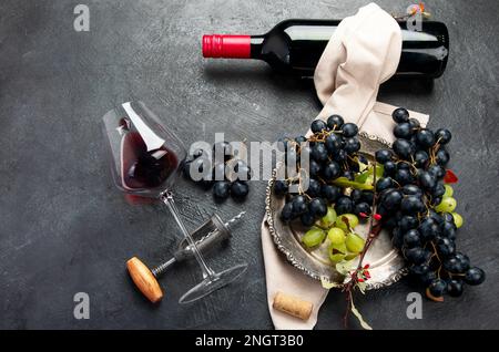 An overhead photo of glasses of red wine with a bottle, grapes, and a vintage corkscew and corks, shot from above on a dark background. Top view. Stock Photo