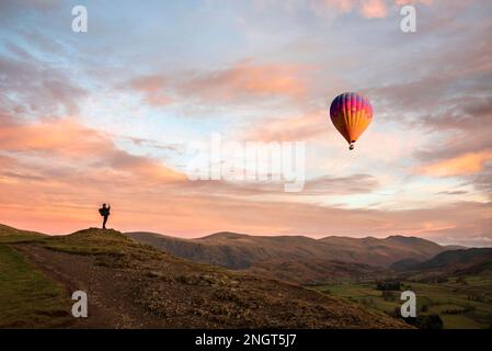 Wonderful sunset landscape image of view from Latrigg Fell towards Great Dodd and Stybarrow Dodd in Lake District with man photographing hot air ballo Stock Photo