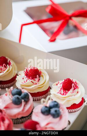 Fresh and delicious cupcakes with cheese cream and fresh berries. Top view of arranged tasty cupcakes in cardboard box isolated on white. Cakes with c Stock Photo