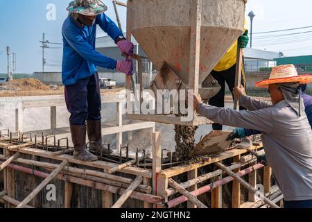 Workers pouring concrete from bucket into formwork at construction site. Stock Photo
