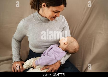 Happy mother taking care of her small baby sleeping in her arms at home - Concept family and motherhood Stock Photo