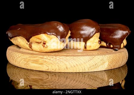 Three chocolate eclairs on a wooden tray, macro, isolated on black background. Stock Photo