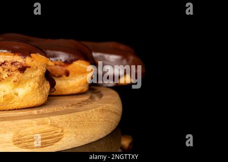 Three chocolate eclairs on a wooden tray, macro, isolated on black background. Stock Photo