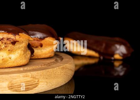 Three chocolate eclairs on a wooden tray, macro, isolated on black background. Stock Photo