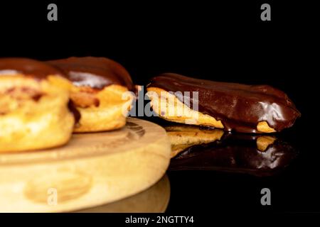 Three chocolate eclairs on a wooden tray, macro, isolated on black background. Stock Photo