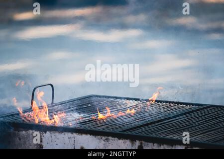 front view closeup detail of metallic large old barbeque grill with fire flames and smoke coming out Stock Photo