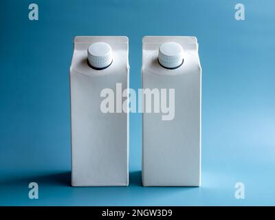 Mockup of two white milk boxes 1 liter with screw cap standing isolated on blue background, vertical style. Photo of white clear empty tall milk boxes Stock Photo