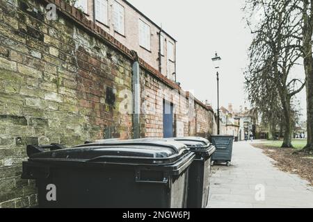 Shallow focus of large retail waste bins seen at the back of shop premises. A pavement and distant people can be seen. Stock Photo