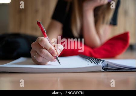 Low angle closeup view of female hand writing in spiral notebook on a living room floor. Doing homework or writing a diary. Stock Photo