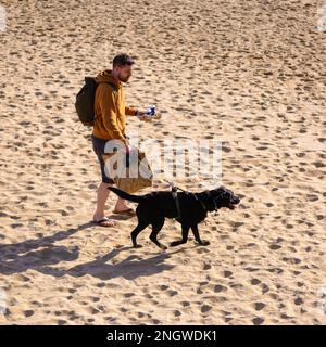 Bournemouth, Dorset, UK, 19th February 2023, Weather. Man and dog on the beach on sunny Sunday as temperatures rise to 14 degrees in the south of England in warm late winter sunshine. Credit: Paul Biggins/Alamy Live News Stock Photo