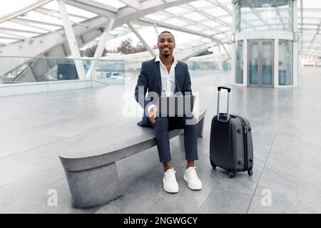 Remote Business. Smiling Black Businessman Working On Laptop While Waiting At Airport Stock Photo