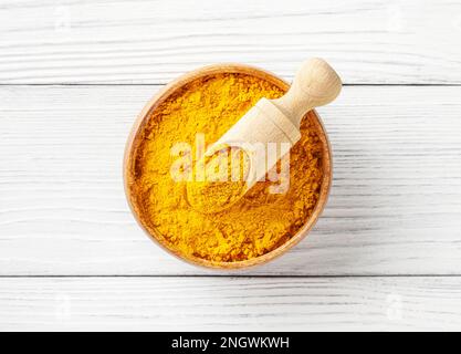 Dry turmeric (curcuma) powder in wooden bowl with scoop on white wooden background Stock Photo