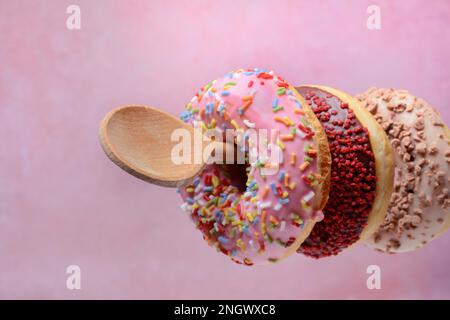 Donuts on wooden spoons against a pink background Stock Photo