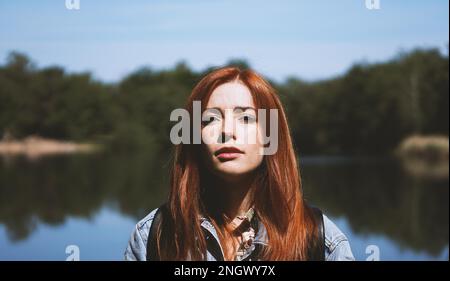outdoorsy young woman standing by lake in harsh light with deep shadows - authentic real people concept Stock Photo