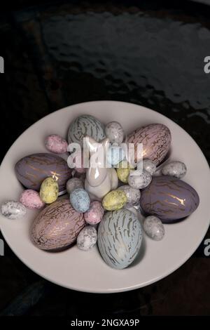 There are a lot of colorful photos lying on a white egg plate and a decorative rabbit on the table Stock Photo
