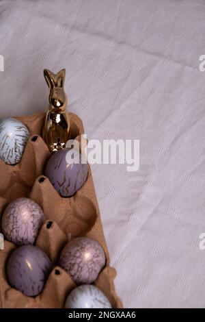 photo of colorful chicken eggs lying in an egg tray and an Easter bunny on a table Stock Photo