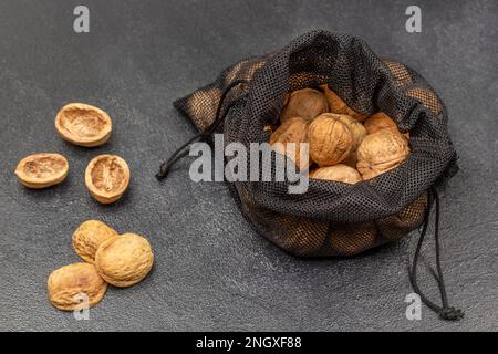 Walnuts in a black reusable bag. Nut shells on the table. Top view. Black background. Stock Photo