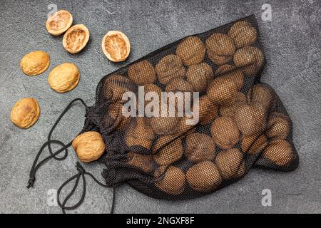 Whole walnuts in a black mesh resealable bag. Nut shell on the table. Flat lay. Black background Stock Photo