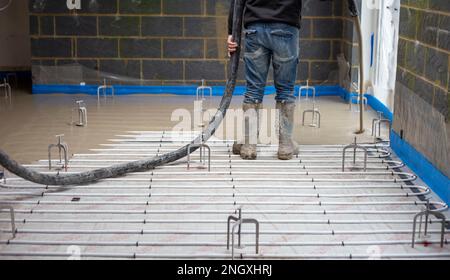 Floor screed being poured out over underfloor heating pipes with leveling tripods in a new build house extension Stock Photo