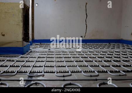 Underfloor heating installation with plastic tubing system in a room under renovation with damaged plaster walls Stock Photo