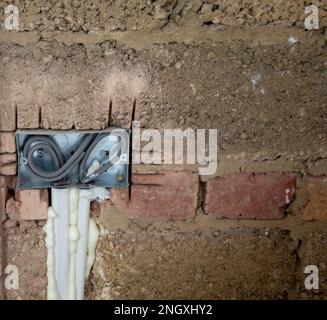 Exposed electrical wiring inside a metal outlet box installed in an unfinished brick wall during construction or renovation work Stock Photo