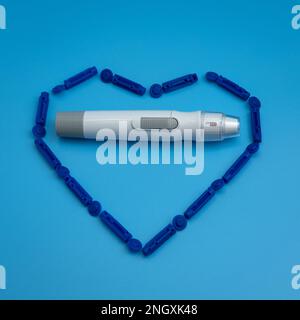 Lancet pen is inside the heart from sterile disposable lancets isolated on blue background. Sugar level blood testing. Treatment of diabetes and glucose controlling concept. Healthcare and medicine.  Stock Photo