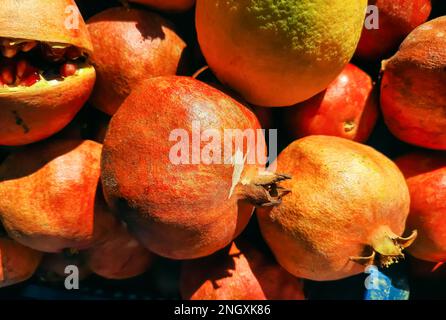 Background of ripe torn pomegranates and an orange in the oriental market. Fruit prepared for making freshly squeezed juice. Stock Photo