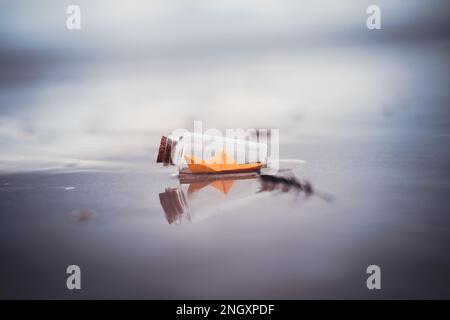 Miniature origami ship in bottle standing on sand at sunrise Stock Photo