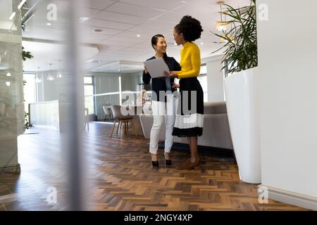 Diverse female colleagues working and talking in office Stock Photo