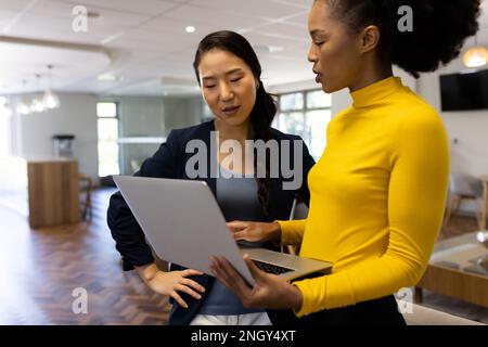 Diverse businesswomen with laptop working and talking in office Stock Photo