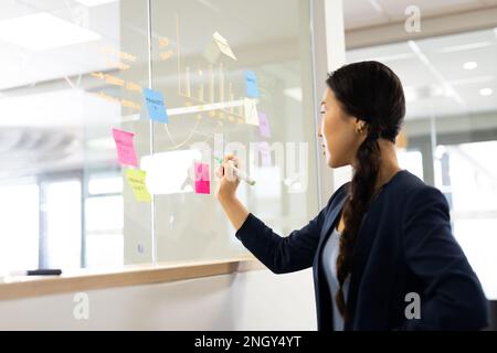 Asian woman brainstorming and writing on glass board in office Stock Photo