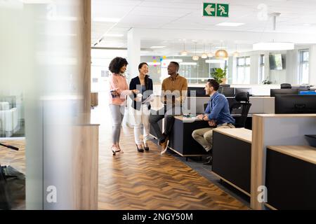 Diverse businesspeople in office talking and laughing Stock Photo