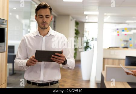 Caucasian businessman with tablet walking in office Stock Photo