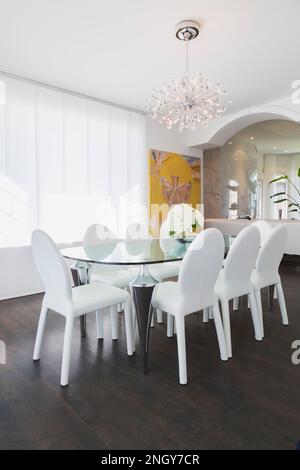 Glass-top and chrome legged dining table with oval back chairs in dining room with dark wood floor inside luxurious home. Stock Photo