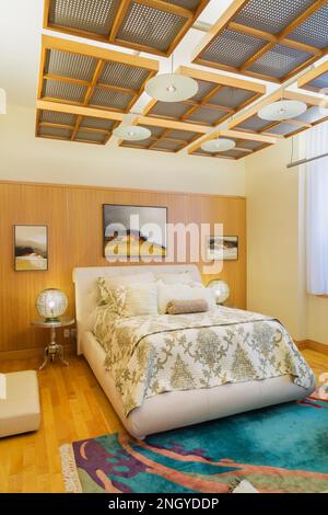 Queen size bed with white leather headboard and bed frame in master bedroom with maple and cherry wood floorboards inside luxurious condominium. Stock Photo