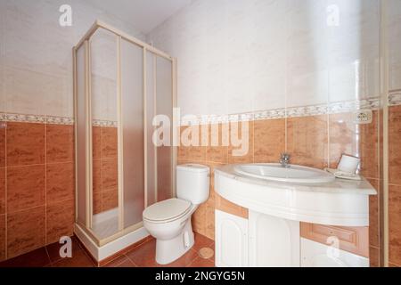 Bathroom with one-piece white resin curvature washbasin cabinet, square shower cabin and brown tiles on the floor and half of the walls Stock Photo