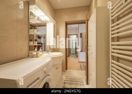 Small bathroom with a white porcelain sink on a wooden and marble cabinet with an integrated mirror and a rail with make-up lights Stock Photo