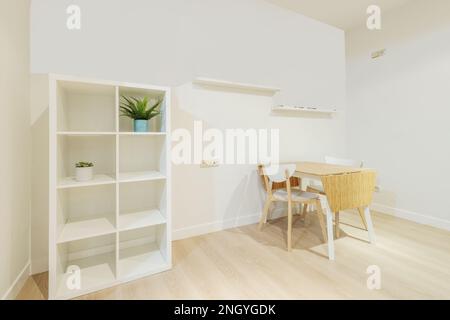 Living room corner with white wooden shelving, shelves on the wall and a wooden folding table with a white frame and matching chairs Stock Photo