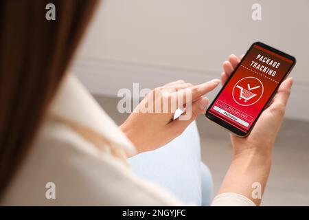 Woman tracking parcel via smartphone indoors, closeup Stock Photo