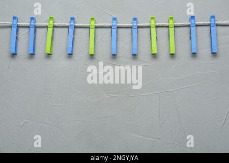 Colorful plastic clothespins and rope on light grey stone background. Space for text Stock Photo