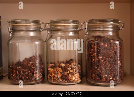 Different types of tea with dried fruit slices in glass jars on wooden shelf Stock Photo