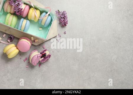 Delicious colorful macarons, marshmallows and lilac flowers on grey table, flat lay. Space for text Stock Photo
