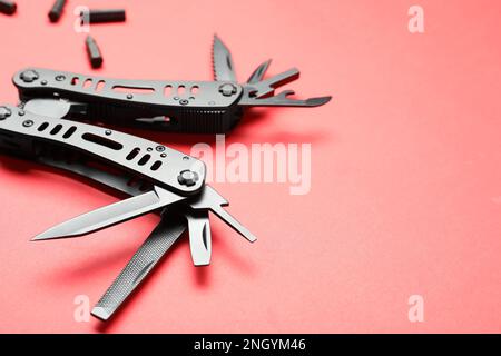 Compact portable black multitool and details on red background, closeup. Space for text Stock Photo