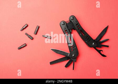 Compact portable black multitool and details on red background, flat lay Stock Photo