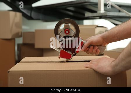 Worker taping cardboard box indoors, closeup view Stock Photo