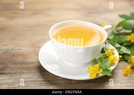 Cup of aromatic celandine tea and flowers on wooden table, closeup Stock Photo