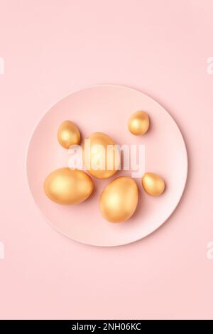 Golden Easter eggs on pastel pink plate. Luxury Easter greeting card in minimal style. Flat lay. Stock Photo